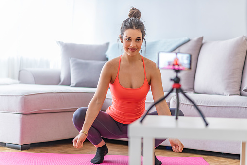 Fitness at home concept. Smiling young woman is sitting on mat with sports equipment at home. Fitness, home and diet concept - smiling teenage girl doing exercise on floor at home. Vlog, Vlogging