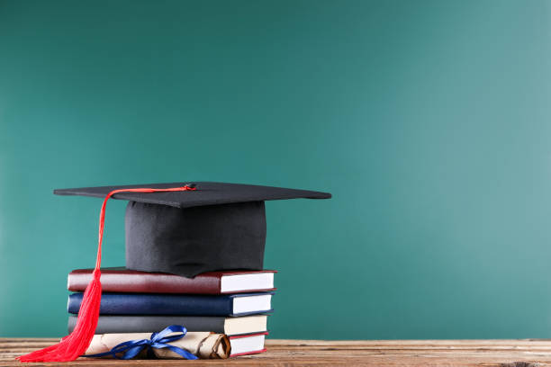 istock Graduation cap with diploma and stack of books on green board background 1140539047