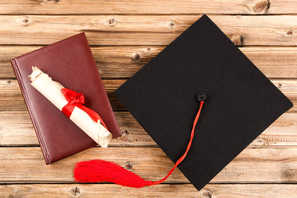 istock Graduation cap with diploma and book on brown wooden table 1140539433