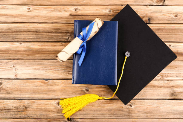 istock Graduation cap with diploma and book on brown wooden table 1140539597