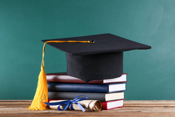 istock Graduation cap with diploma and stack of books on green board background 1140540832