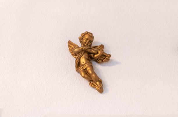 Gold cherub laying flat on white surface playing a small harp.