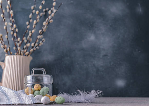 istock Willow branches in a vase on a gray background and chocolate eggs for the Easter holiday. A bunch of sprout. Card with flowers and sweets. Copy space. 1140557956