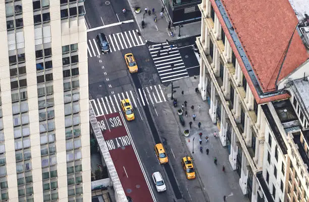 Photo of New York city street with yellow taxis and people walking. Cabs, cars and pedestrians crossing crosswalk. Busy NYC Downtown traffic. Aerial view.