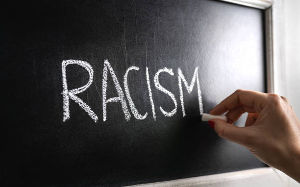 Hand writing the word racism on blackboard. Stop hate. Against prejudice and violence. Lecture about discrimination in school. Hand writing the word racism on blackboard. Stop hate. Against prejudice and violence. Lecture about discrimination or stereotypes in school. racism photos stock pictures, royalty-free photos & images