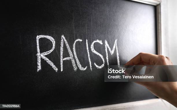 Hand Writing The Word Racism On Blackboard Stop Hate Against Prejudice And Violence Lecture About Discrimination In School Stock Photo - Download Image Now