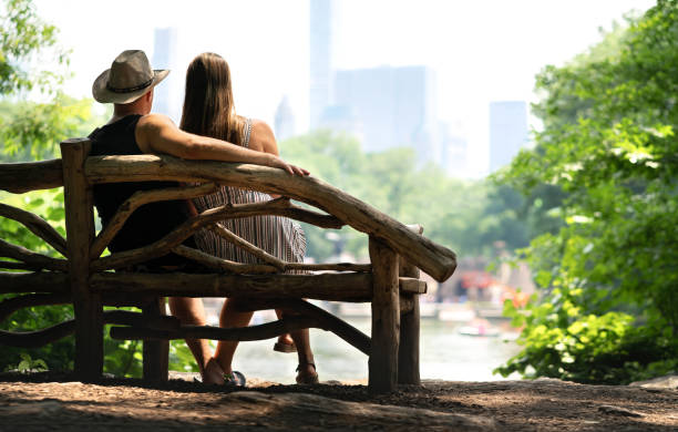 istock Couple sitting on a park bench and having a romantic first date. Lovers with romance and trust. Back view of happy man and woman watching the buildings in Manhattan, New York City, Central Park. 1140559928