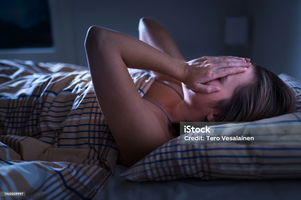 Insomnia, sleep apnea or stress concept. Sleepless woman awake and covering face in the middle of the night. Lady can't sleep. Nightmares or depression. Suffering from headache. Insomnia, sleep apnea or stress concept. Sleepless woman awake and covering face in the middle of the night. Lady can't sleep. Nightmares or depression. Suffering from headache or migraine. Horror Stock Photo