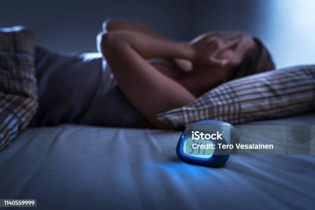 Sleepless Woman Suffering From Insomnia Sleep Apnea Or Stress Tired And Exhausted Lady Headache Or Migraine Awake In The Middle Of The Night Frustrated Person With Problem Alarm Clock Stock Photo - Download Image Now