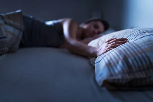 Photo of Single woman sleeping alone in bed at home. Lonely lady missing husband or boyfriend. Hand on pillow. Solitude, infidelity or heartbreak concept. Loneliness and sorrow after break up.