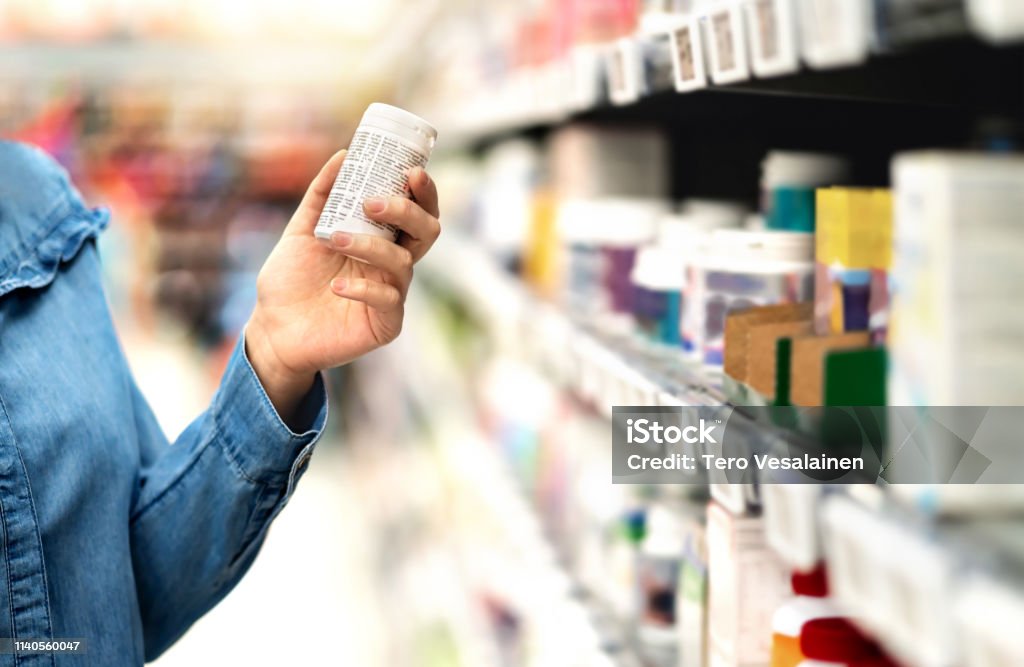 Customer in pharmacy holding medicine bottle. Woman reading the label text about medical information or side effects in drug store. Patient shopping pills for migraine or flu. Customer in pharmacy holding medicine bottle. Woman reading the label text about medical information or side effects in drug store. Patient shopping pills for migraine or flu. Vitamin or zinc tablets. Nutritional Supplement Stock Photo