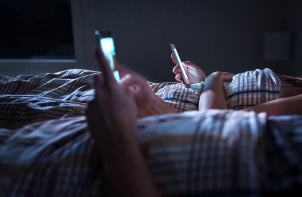 Bored distant couple ignoring each other lying in bed at night while using mobile phones. Smartphone addict. Obsessed and distracted man and woman texting. Addiction to social media. stock photo