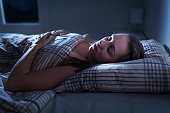 Calm and peaceful woman sleeping in bed in dark bedroom. Lady asleep at home in the middle of the night. Pillow, blanket and moonlight. Nightmare or sleep apnea.
