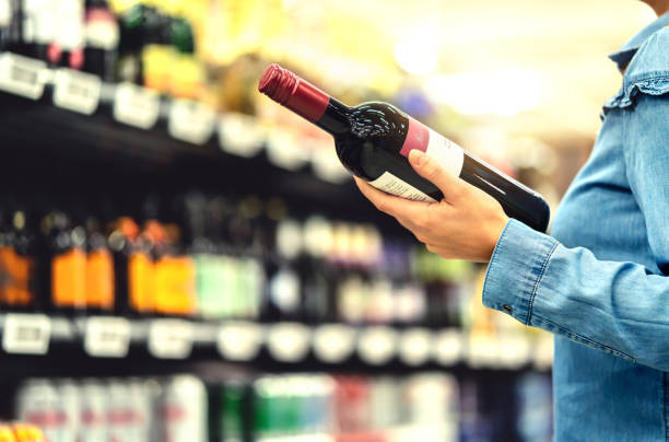 alcohol shelf in liquor store or supermarket. woman buying a bottle of red wine and looking at alcoholic drinks in shop. happy female customer choosing merlot or sangiovese. - department store imagens e fotografias de stock