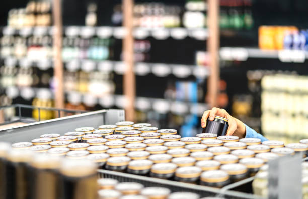 retail worker filling shelf with drinks in grocery store or customer taking can of beer or soda. staff at supermarket stocking shelf with alcohol or doing inventory. woman buying liquor. - department store imagens e fotografias de stock