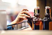 Hand taking bottle of beer from shelf in alcohol and liquor store. Customer buying cider or supermarket staff filling and stocking shelves. Retail worker working.