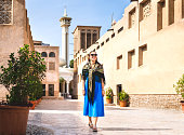 Woman walking in old Dubai, UAE. Traditional Arab street and mosque. Female tourist in historical Al Fahidi neighbourhood wearing dress. Tourism in heritage district. Happy vacation.