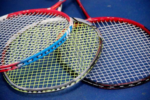 three badminton rackets lying ropna floor in the gym badminton rackets lying on the blue wooden floor of the sports field. Three badminton rackets lying ropna floor in the gym, closeup. badminton racket stock pictures, royalty-free photos & images