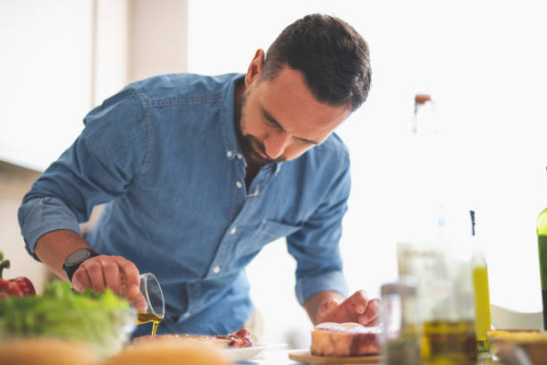 istock Focused young man cooking meat while standing near kitchen table 1140563981