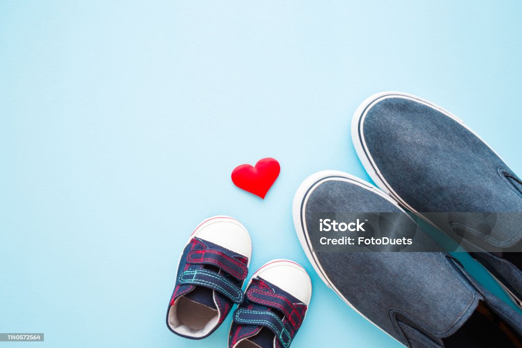 Father and son shoes with red heart shape on pastel blue background. Love concept. Empty place for sentimental, lovely, cute text, quote or sayings. Flat lay. Father's Day Stock Photo