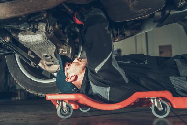 Car Mechanic Repair Job Caucasian Car Mechanic on a Creeper Performing Vehicle Repair Inside Authorized Auto Service Station. mechanic working under car stock pictures, royalty-free photos & images