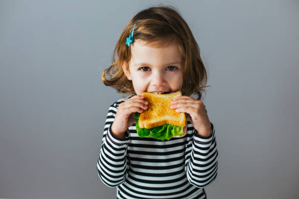 A young girl biting into a sandwich.