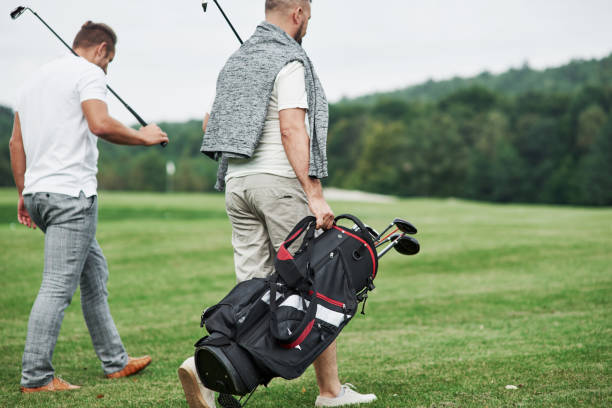 istock Back view. Two friends walking through the lawn with golf equipment and talking 1140575493