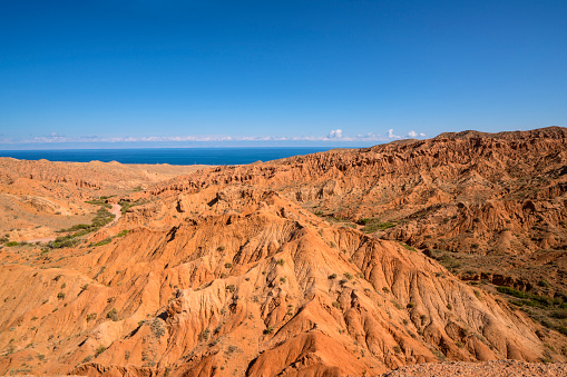 Colorful rocky landscape, created by wind making amazing formations called The Fairy Tale Canyon / Skazka Canyon,   which is not far from small town Bokonbayevo which is located in the Southern shore of lake Issyk-Kul, which is in background. Kyrgyzstan.