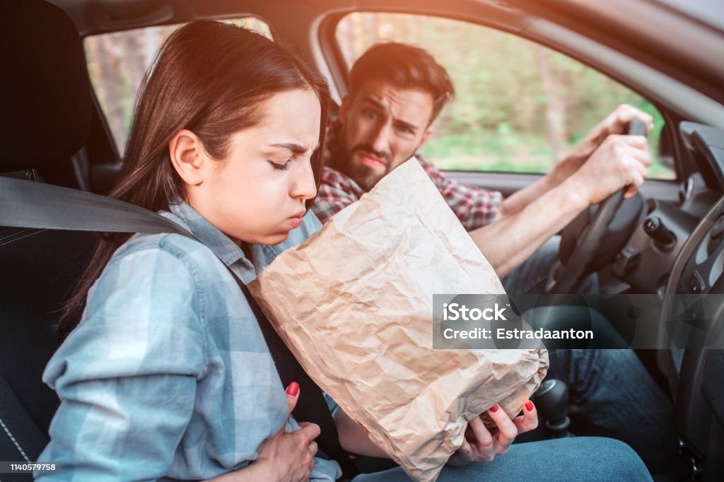 A picture of sick girl holding a bag and trying to vomit into it. She feels bad. Girl is holding her hand on stomach. Guy is looking at her with sight full of disgution. A picture of sick girl holding a bag and trying to vomit into it. She feels bad. Girl is holding her hand on stomach. Guy is looking at her with sight full of disgution Illness Stock Photo