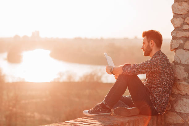 istock Young man reading a book outdoors in sunset 1140587804