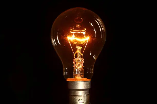 Clear glass electric lightbulb dimmed to enable it's tungsten filament to be seen isolated on a black background
