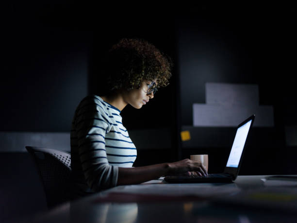 Concentrated businesswoman working late hours with her laptop A businesswoman staying late hours in the office concentrating on her work sitting with a laptop and typing. working overtime stock pictures, royalty-free photos & images