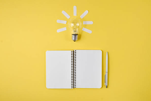 istock Financial planning table top with pen, notepad, light bulb on yellow background. Concept brainstorming and new idea 1140602308