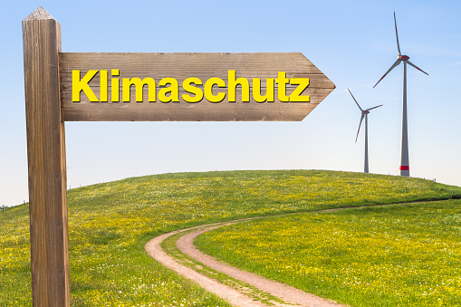 Sign with the Word Climate Protection in German and Wind Turbines in the Background