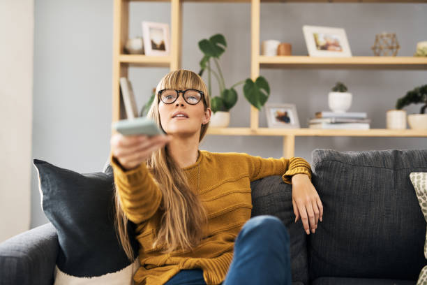 What have I missed out on this week? Shot of a young woman watching television on the sofa at home control point stock pictures, royalty-free photos & images