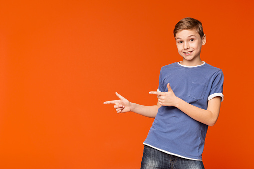 Cute little boy pointing away at empty space on orange studio background
