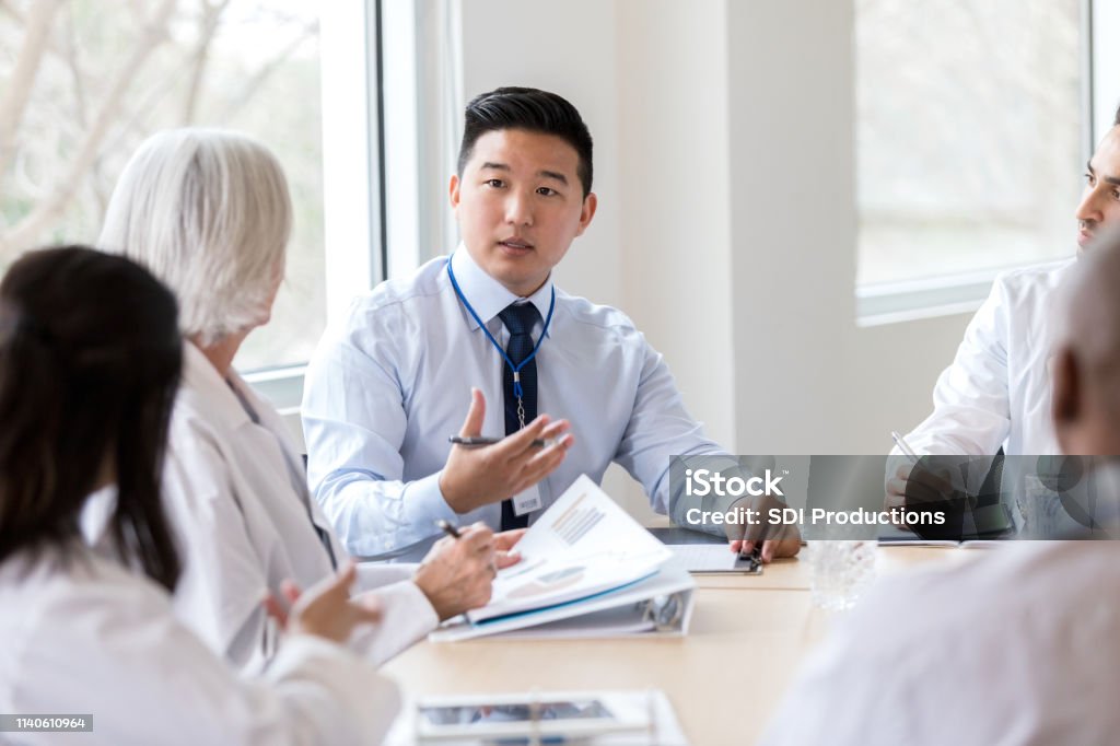 Serious hospital executive talks during meeting Male hospital administrator gestures while discussing a serious topic during a staff meeting. Healthcare And Medicine Stock Photo