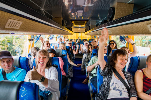 Excited to Travel A front-view shot of a large multi-ethnic group of tourists celebrating on a coach bus, they are smiling and raising their arms with excitement, they are ready to begin their journey. bus stock pictures, royalty-free photos & images