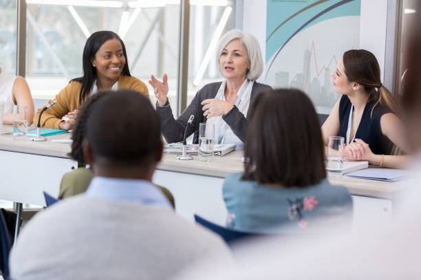 A mature woman explains the focus of the panel During her presentation, a mature woman introduces her fellow panelists and explains the focus of the conference. summit meeting photos stock pictures, royalty-free photos & images
