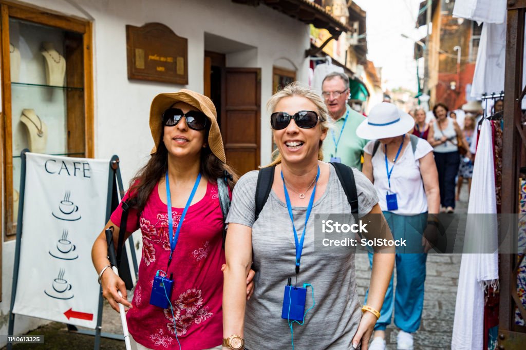 Touring India A front-view shot of a multi-ethnic group of tourists walking down a narrow street in Kerala, India. Some of the tourists are visually impaired and can be seen using a blind person's cane and holding onto a friends arm for guidance. Tourism Stock Photo