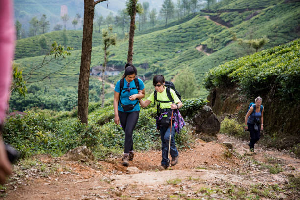 Assisting a Friend Woman supporting a visually impaired woman on a hike in Munnar, India. They are both smiling and wearing backpacks. The visually impaired woman is using a cane. disabled person hiking outdoors stock pictures, royalty-free photos & images