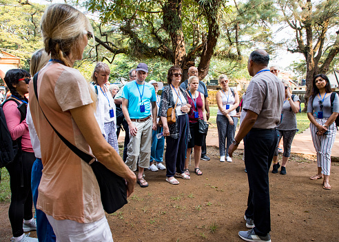A front-view shot of a group of tourists listening to a male tour guide speaking in a rural area in Kerala, India.