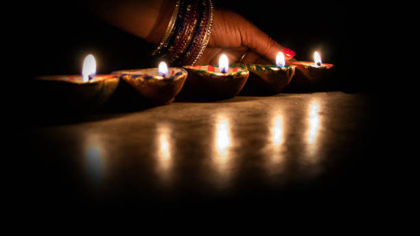 istock Hand holding a matchstick lighting diya lamps during diwali celebration - Image 1140622662