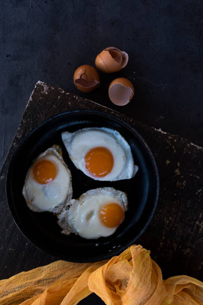 istock Overhead view of  fried eggs in black baking pan on dark background 1140624749