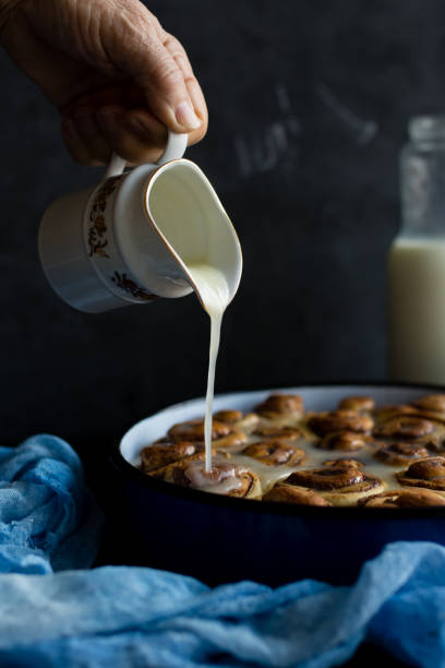 istock Baker putting sugar glaze syrup on to baked cinnamon buns 1140625100