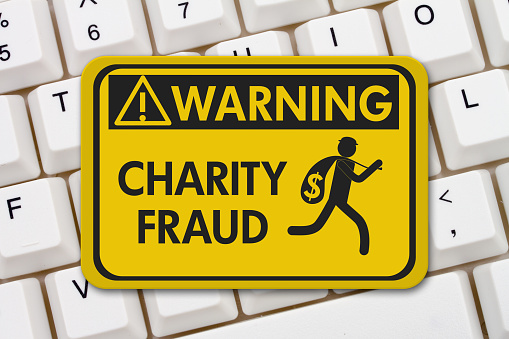 Charity Scam warning sign, A yellow warning sign with text Charity Fraud and theft icon on a keyboard