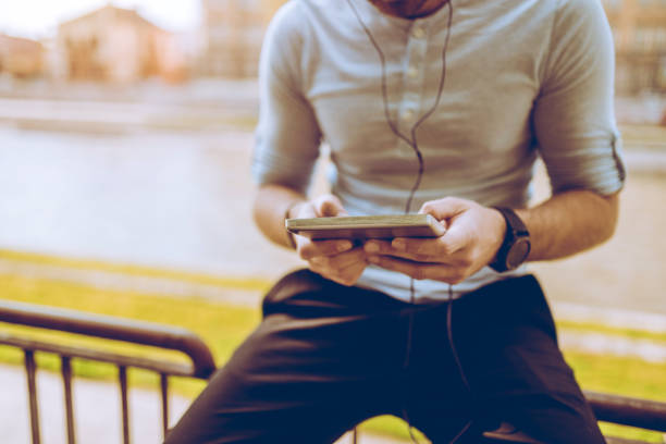 Young man is listening to music on digital tablet by the riverbank