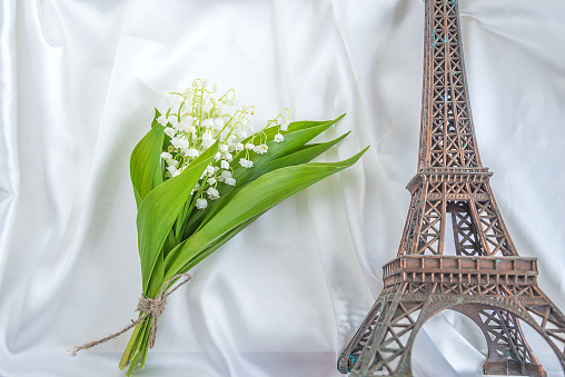 Bouquet of lilies of the valley and Eiffel Tower statue on the white silk background
