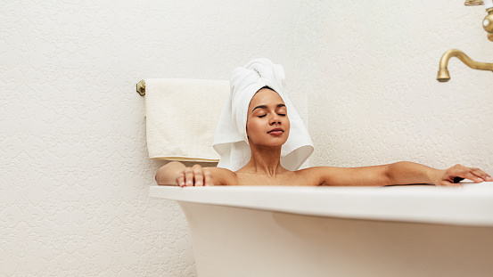 Woman with white towel on her head relaxing in bath with eyes closed
