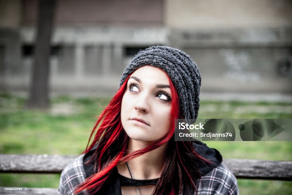 Homeless girl, Young beautiful red hair girl sitting alone outdoors with hat and shirt feeling anxious and depressed after she became a homeless person close up portrait Adults Only Stock Photo